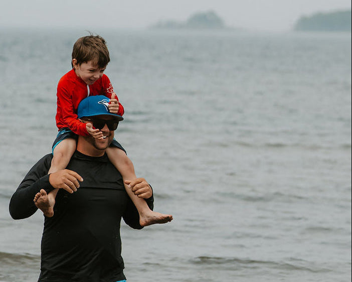 Man carrying a child on his shoulders by a body of water