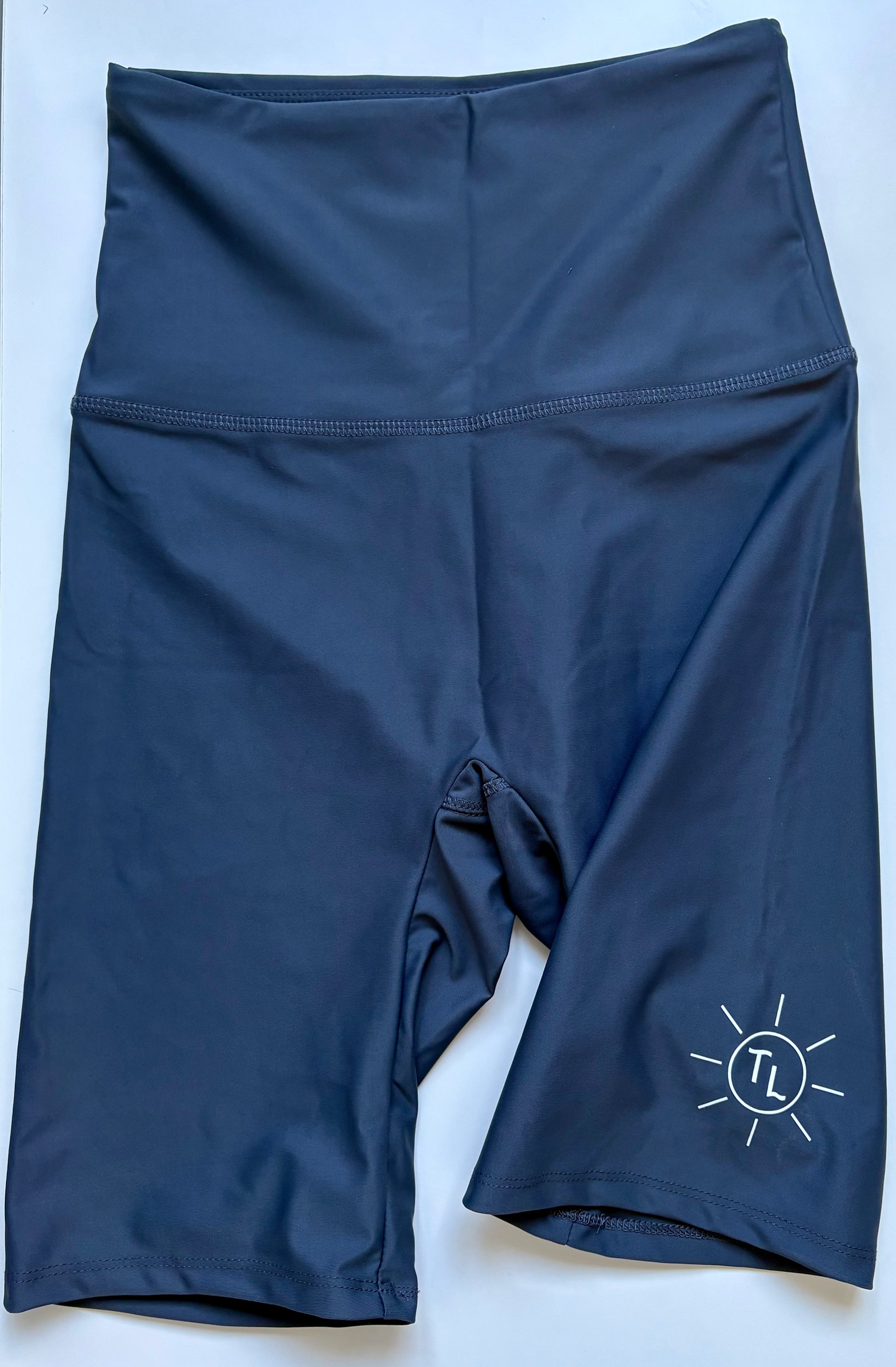 A pair of charcoal grey women's UPF 50+ swim shorts with a high waist and above knee-length fit, featuring a small white logo on the lower left leg.