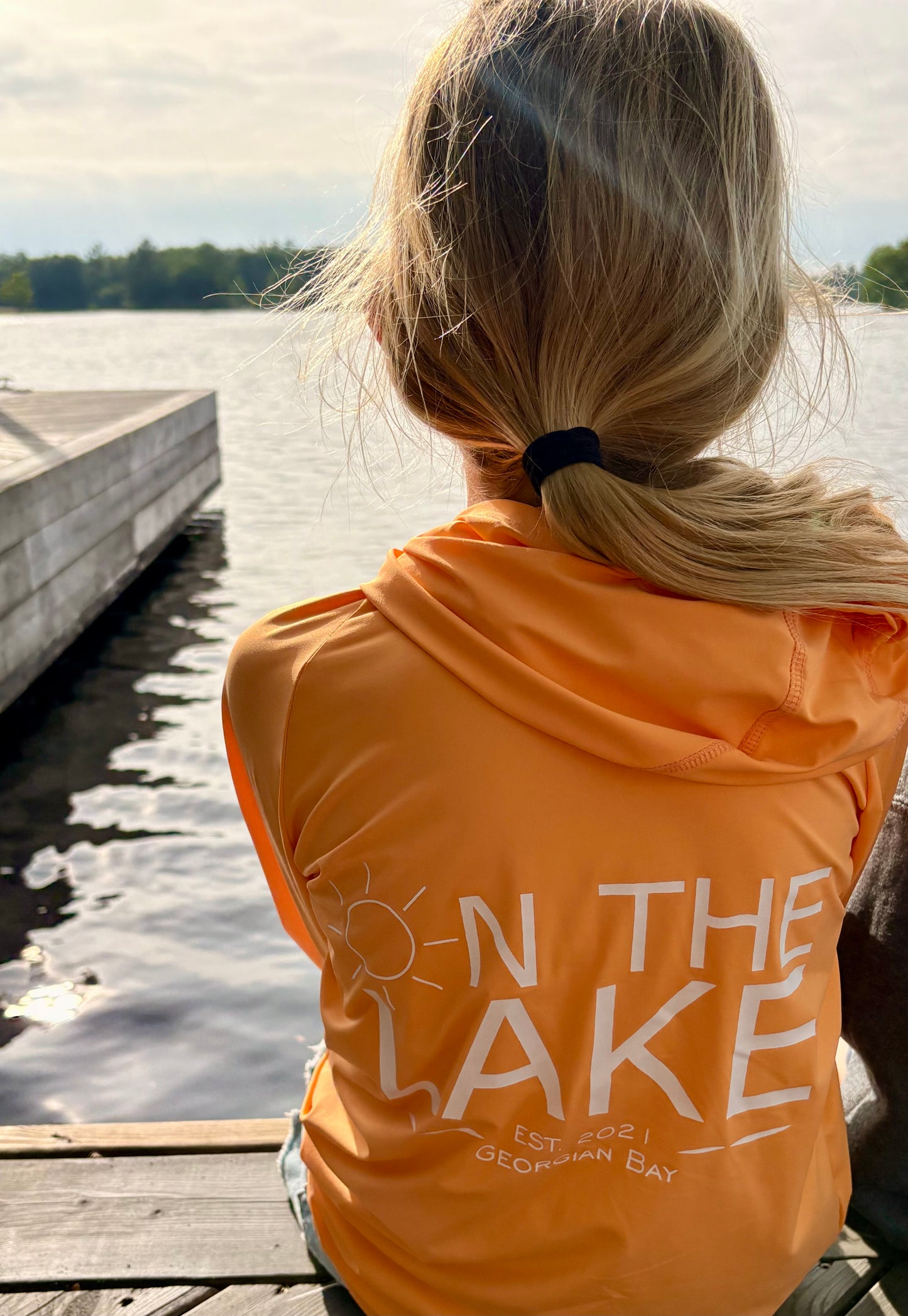 Child fishing off the dock while wearing peach colour quick dry UPF 50+ sun protection hoodie Georgian Bay Edition across the back